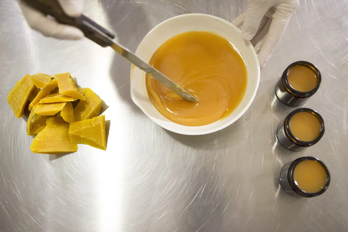 Golden beeswax pieces and a small pot of melted wax