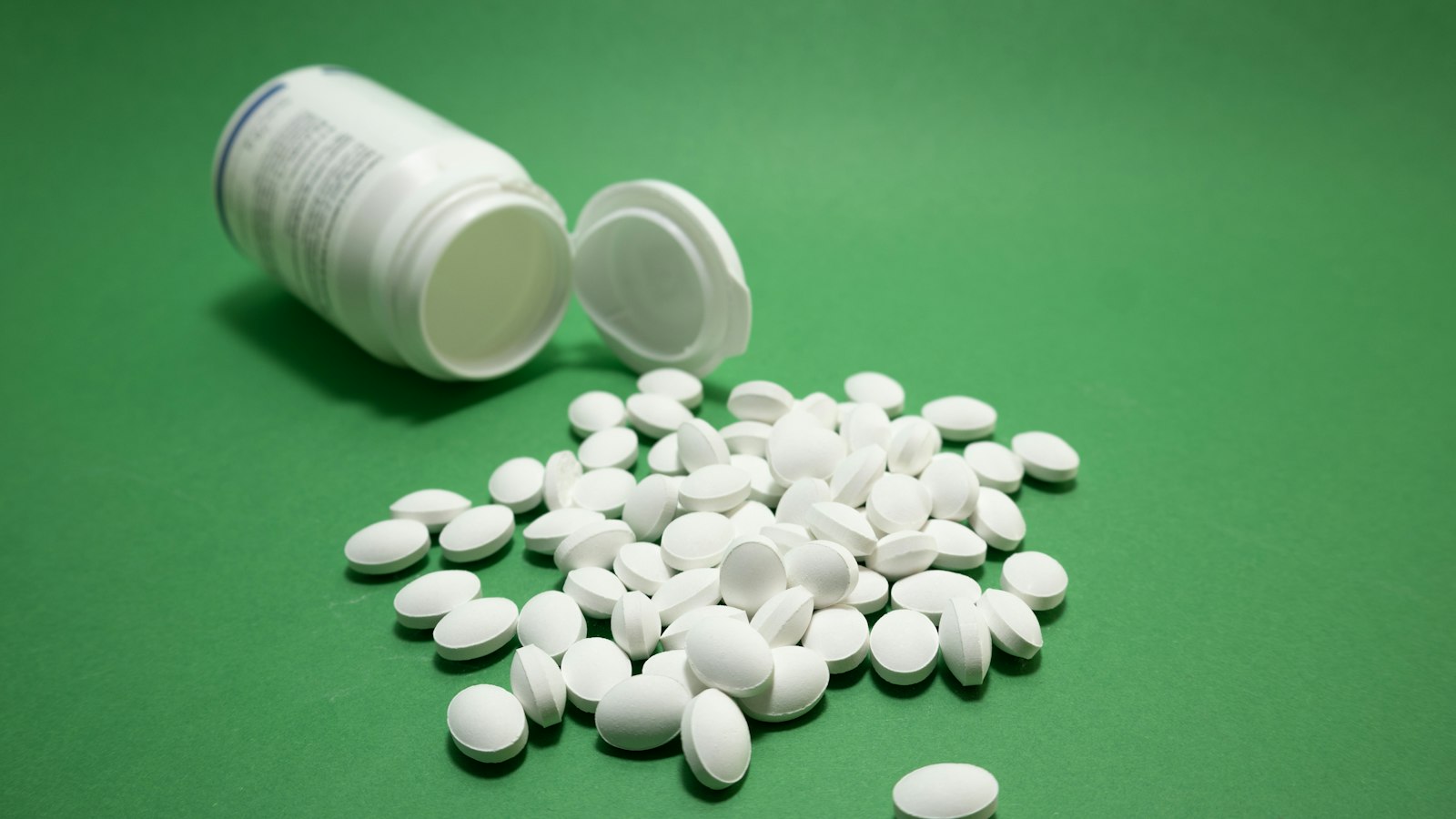 Ca-AKG side effects: white supplement tablets spilled from an open bottle