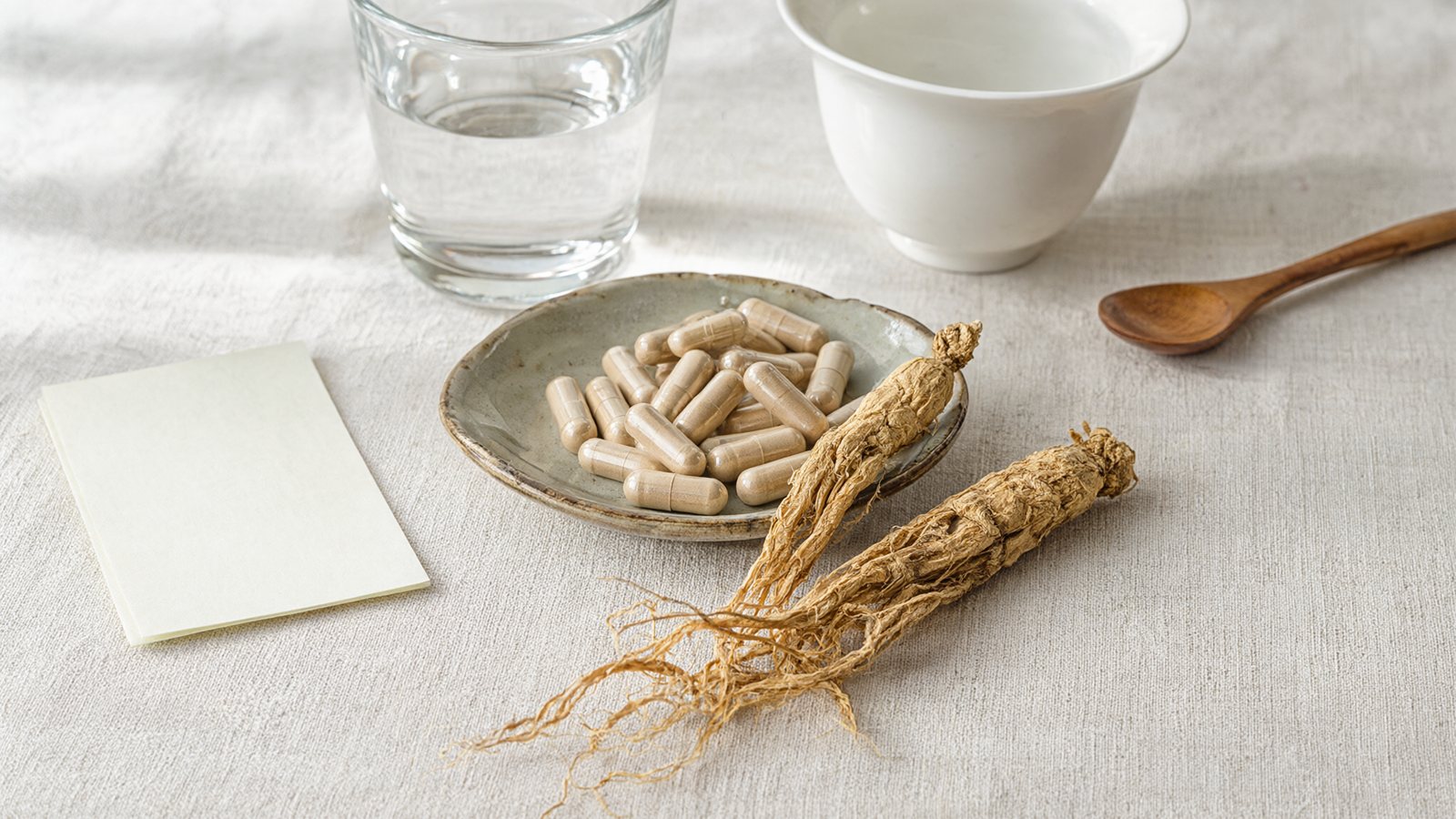 Ginseng side effects: dried Korean red ginseng roots beside ginseng capsules and a glass of water